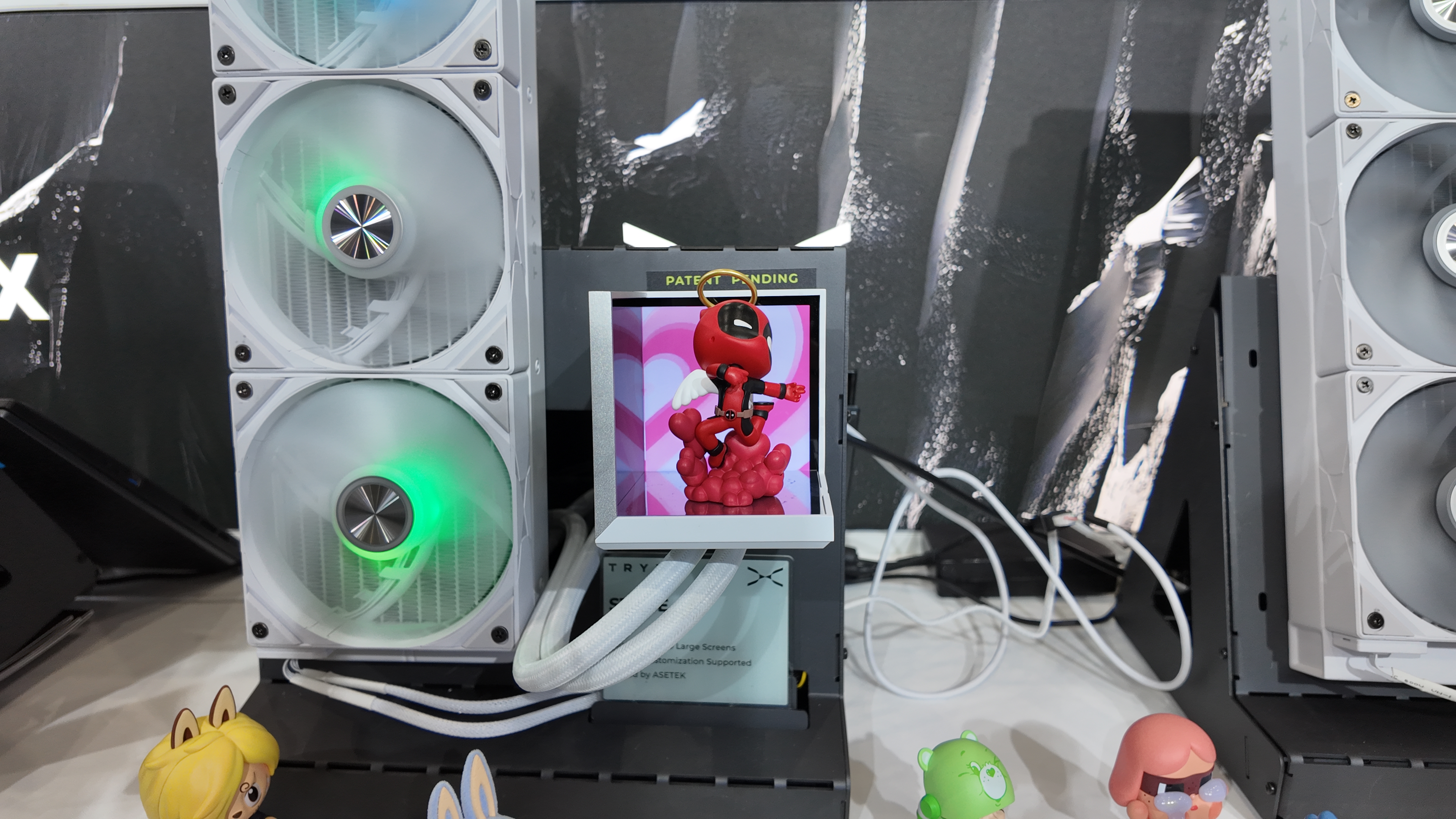 Tryx's 'Stage' display shelf intended for the inside of a PC case. It includes two small HD screens. A small Deadpool figure is perched on top of the shelf, surrounded by the small HD screens on two sides. This display was photographed at Computex 2025.