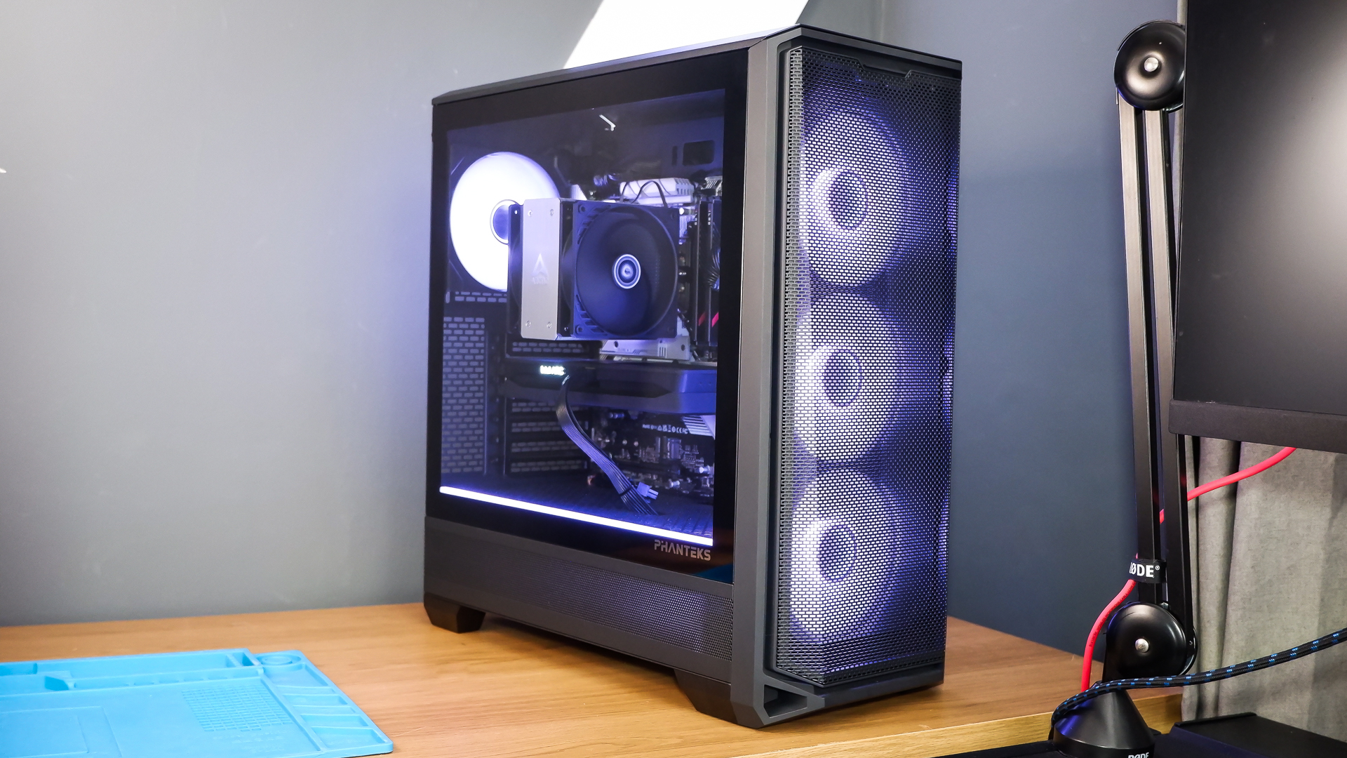 A gaming PC sat on a desk with purple RGB lighting on the fans and light bar enabled.