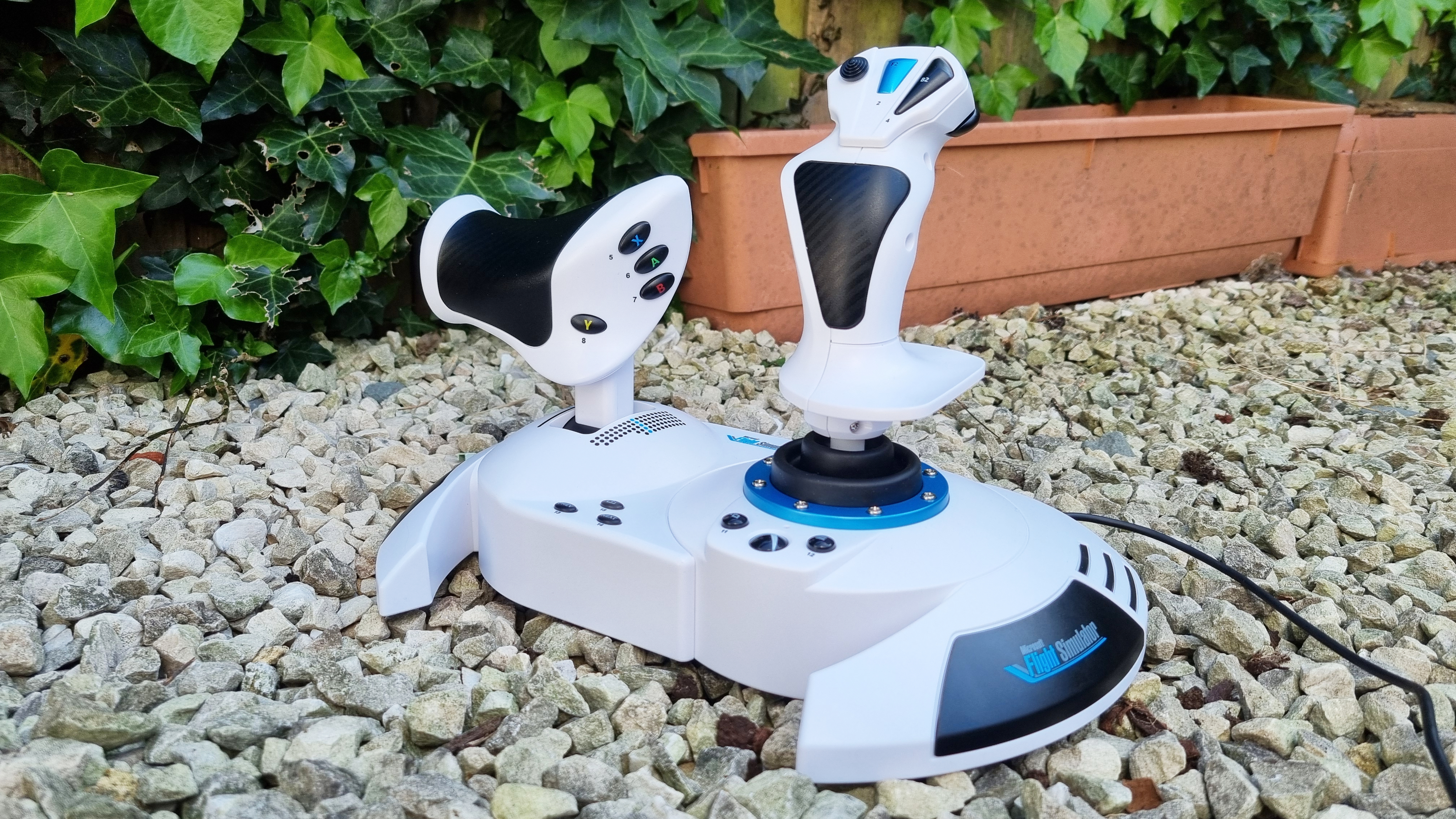 The Thrustmaster T.Flight HOTAS One Microsoft Flight Simulator Edition on white gravel with foliage in the background