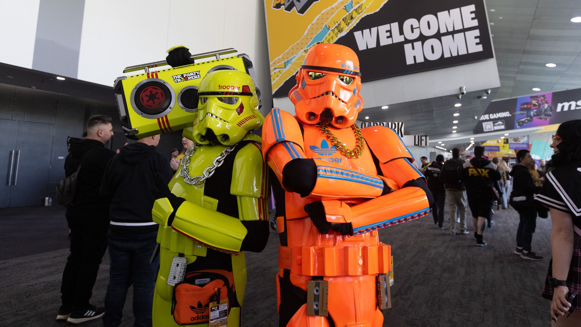 Two brightly colored stormtroopers dressed like Run-DMC stand in front of PAX Australia's WELCOME HOME banner.